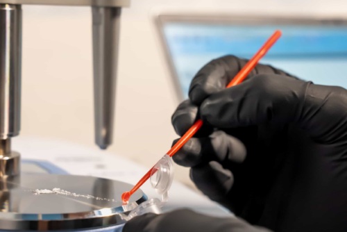 Close of photo in a lab of a gloved hand scooping a white substance into a test tube.