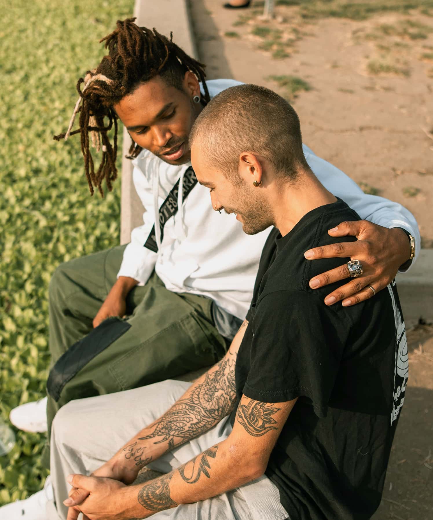Friends sitting in a park, one supporting the other.